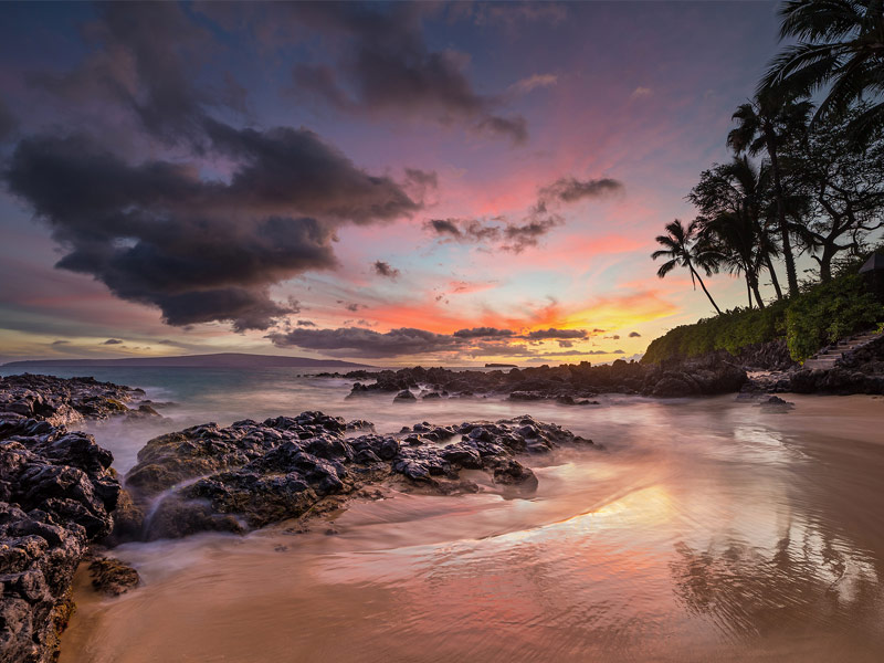 rocky shorline with waves crashing and beautiful sunset in distance