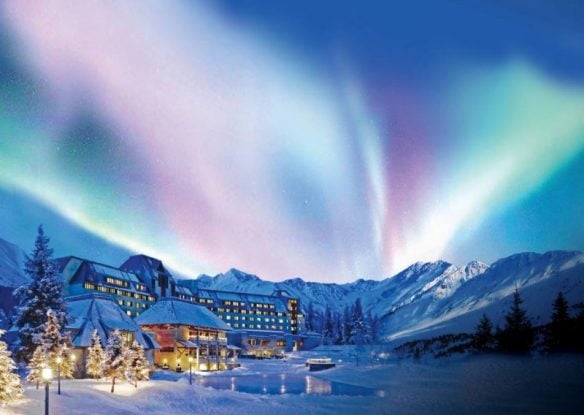 Northern lights shining bright over resort in middle of snow-covered landscape