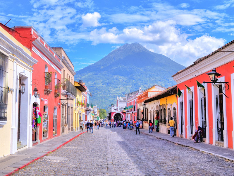 colorful houses line a cobblestone tree with pedestrians walking and a mountain in the distance