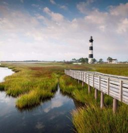 wooden pier over wetlands with lighthouse in distance