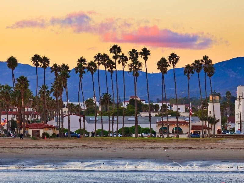 Tall, skinny palm trees sit behind beach with mountain silhouette in background