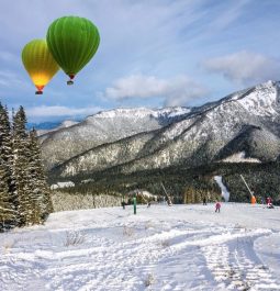 two hot air balloons fly above snowy ski resort