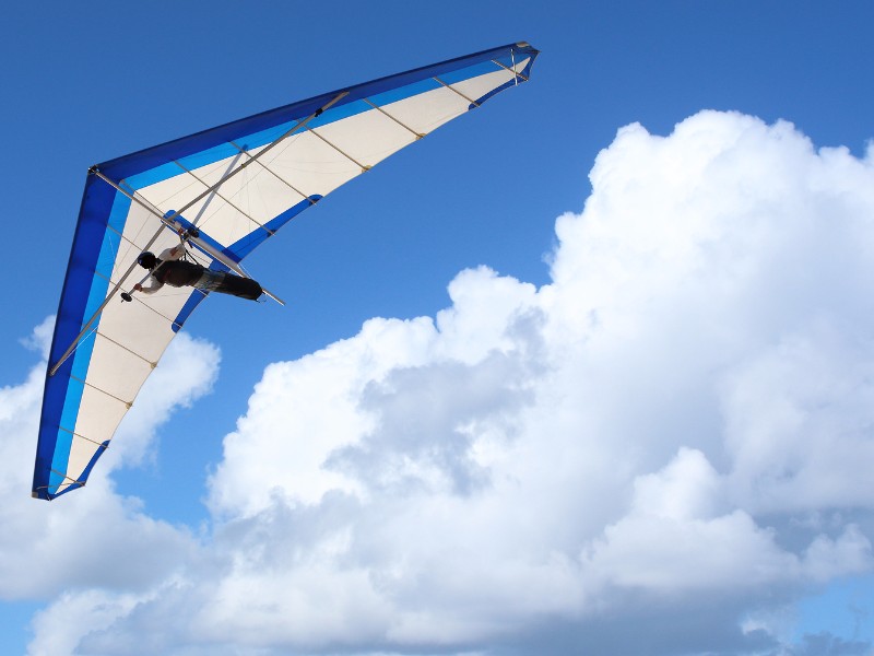 Hang Glider flying through the sky white puffy clouds