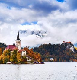 island in the middle of lake with a church on it and fall foliage surrounded it