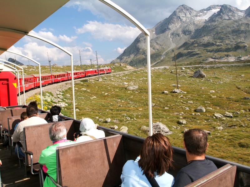 People sitting on the Bernina express train and admiring the scenic view on the Swiss alps