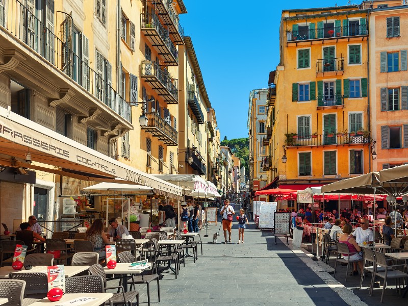 People sitting in outdoor restaurants on narrow street in Old town of Nice 