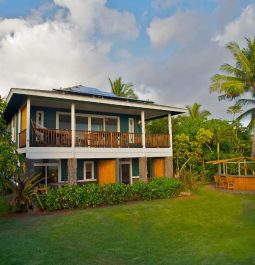 two-story bungalow style home with balconies surrounded by lush vegetation and green lawn