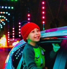 Smiling young boy sticking head out of car window admiring holiday drive-thru light display