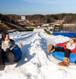 two young girls sit in snow tubes at top of mountain tubing area