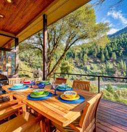 Beautiful wooden deck with teak dining set overlooking river and tree-covered mountain