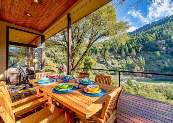 Beautiful wooden deck with teak dining set overlooking river and tree-covered mountain
