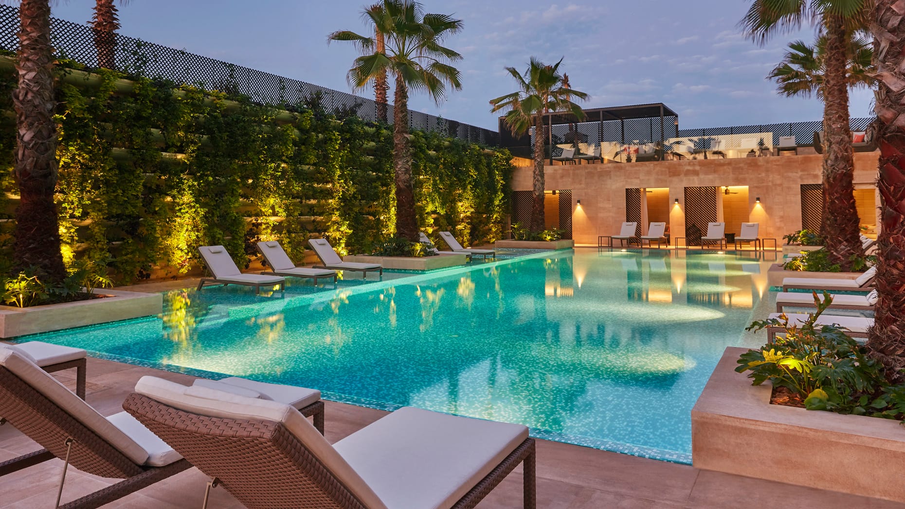 Swimming pool surrounded by sun loungers lit up in the evening