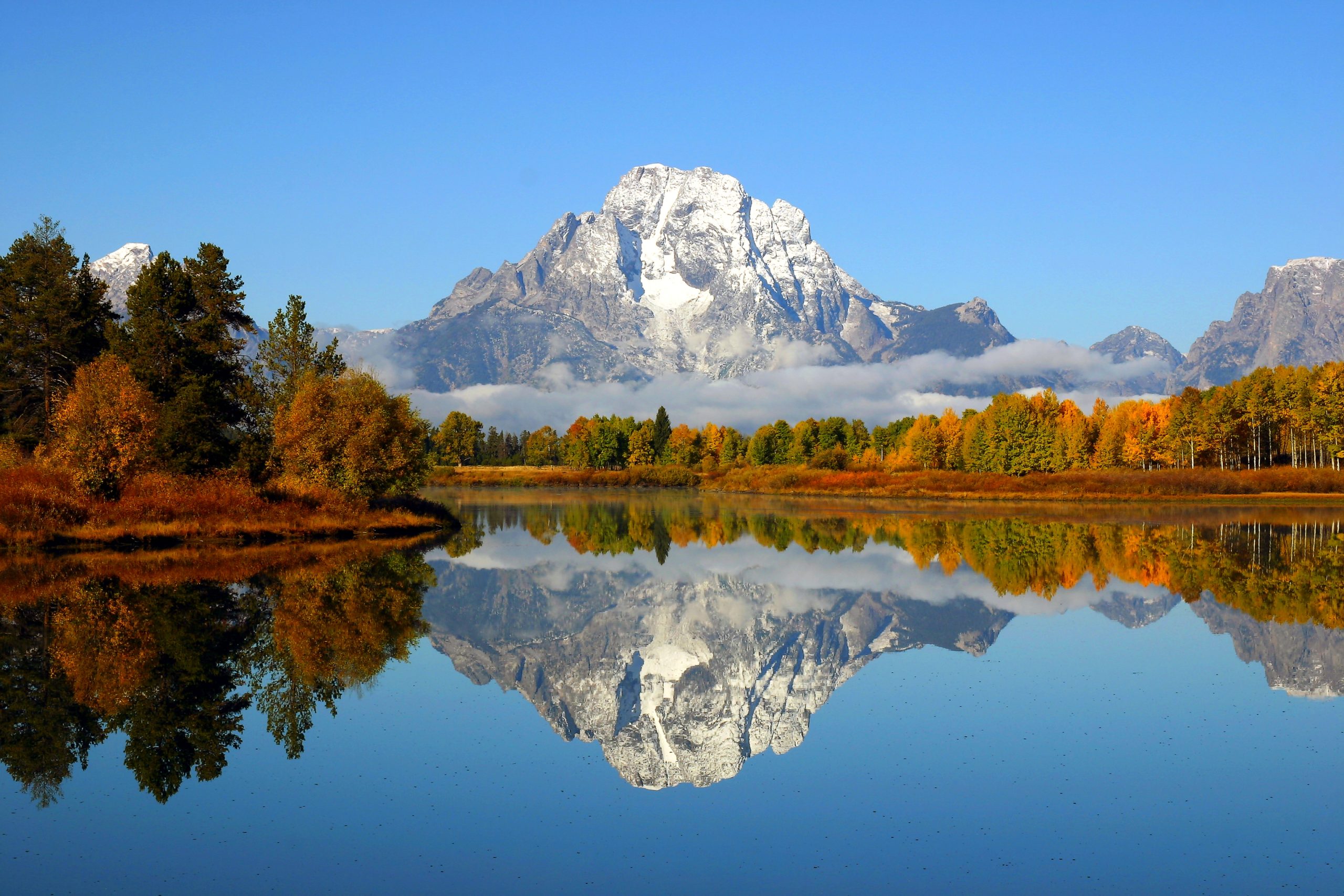 Grand Tetons reflected in still water with fall foliage